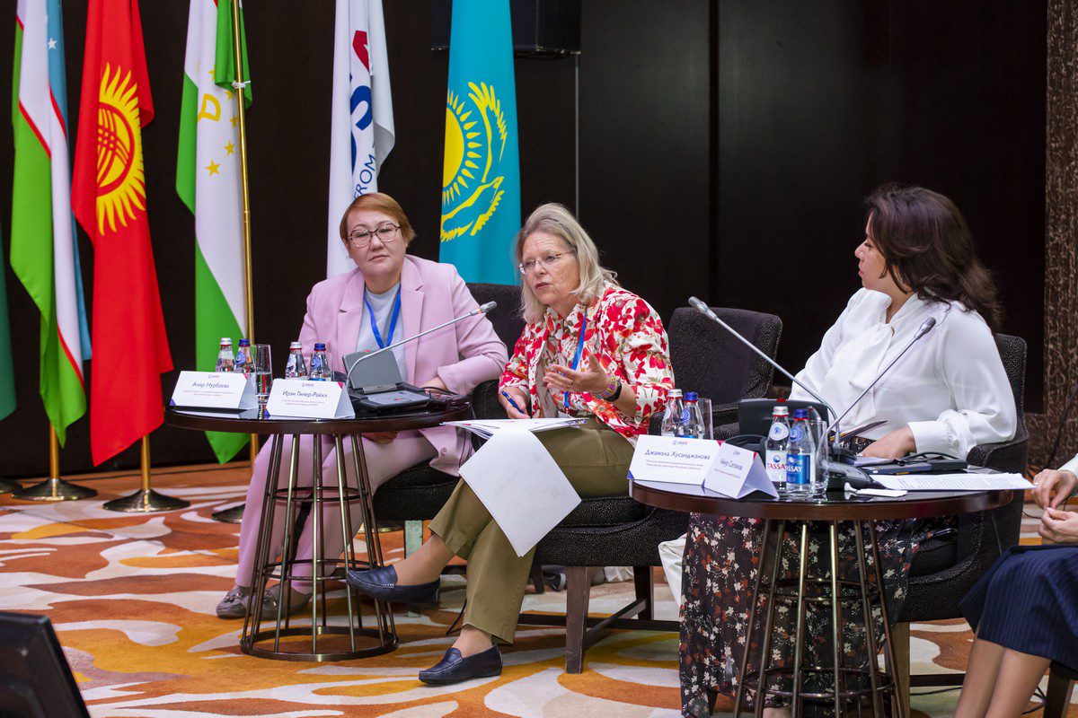 Three women on stage, with flags behind them