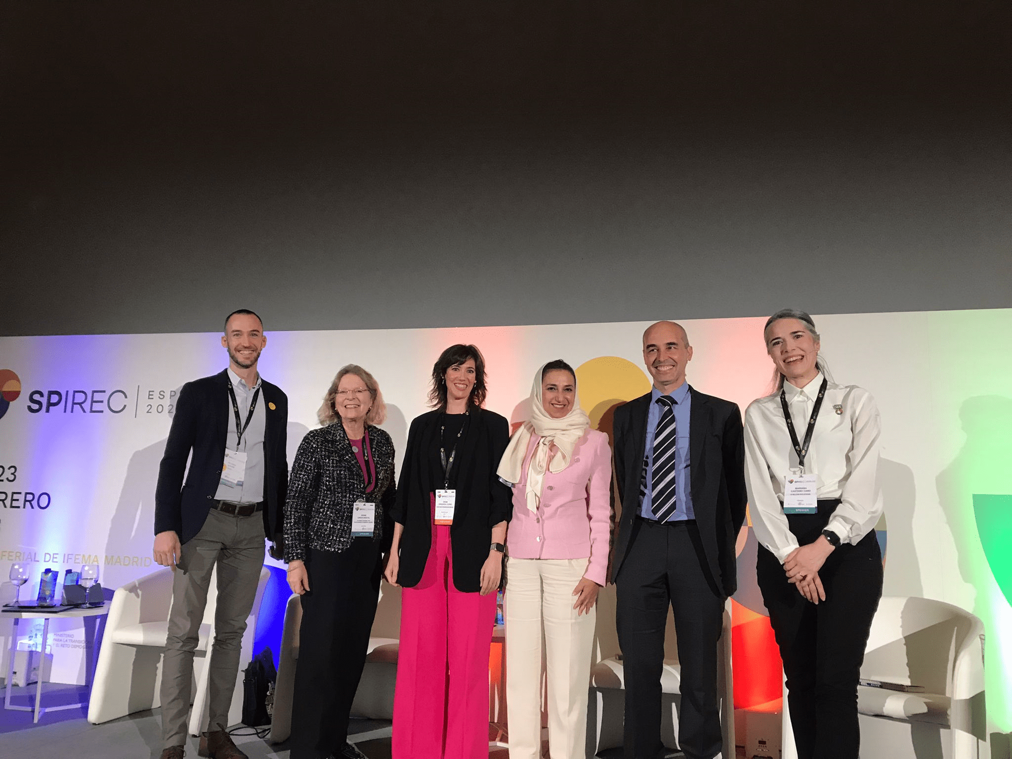 Panellists standing on stage with conference poster as a backdrop