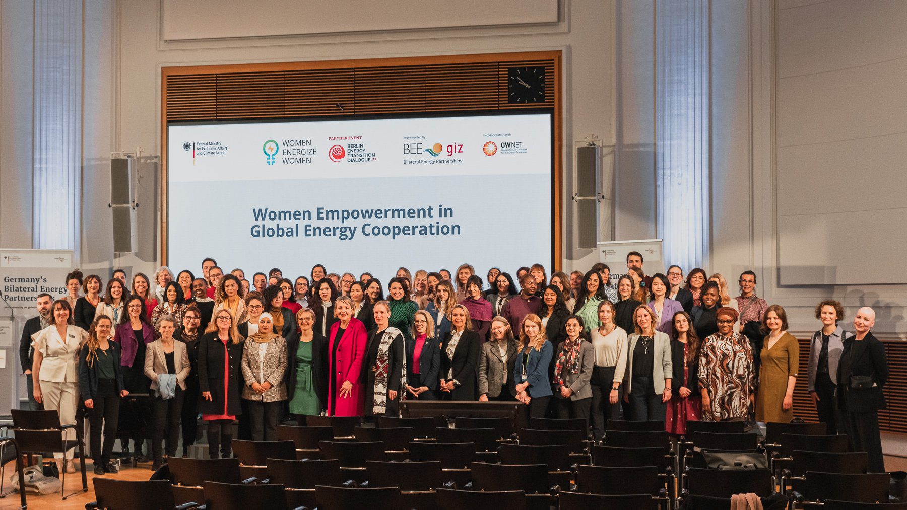 Event participants stand together on stage with the event poster as a backdrop